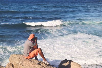 High angle view of man photographing while sitting on rocks at beach