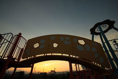 Low angle view of illuminated amusement park against sky at sunset