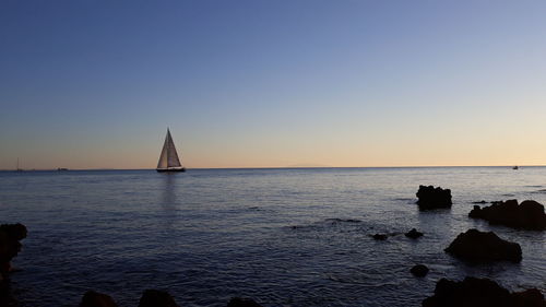 Sailboat in sea against clear sky during sunset