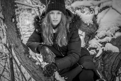 Portrait of smiling young woman sitting on snow covered tree