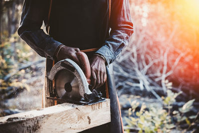 Midsection of carpenter cutting wood outdoors