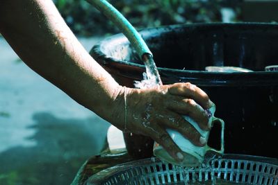 Cropped hands of person cleaning utensils with water