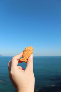 Close-up of hand holding blue sea against clear sky