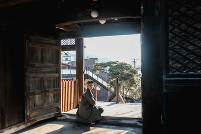 Rear view of woman sitting by door against sky