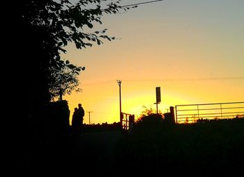 Silhouette people by tree against orange sky