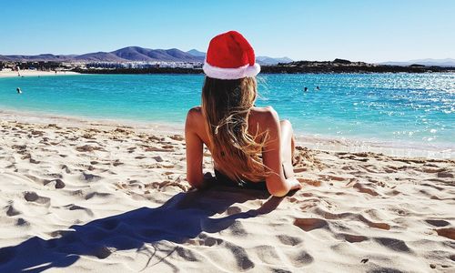 Rear view of woman wearing santa hat sitting at beach