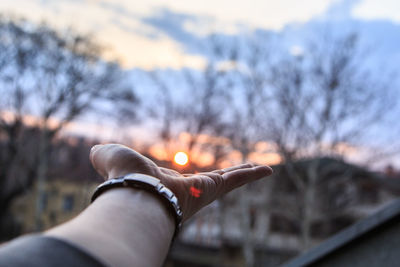 Close-up of hand against sky during sunset