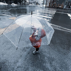 High angle view of girl holding umbrella standing on wet street