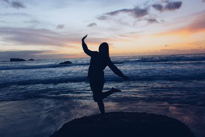 Silhouette woman standing on beach against sky during sunset