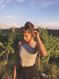 Thoughtful woman standing by plants against sky during sunny day