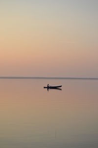 Person sitting in boat against sky during sunset