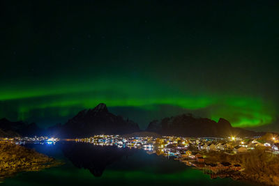 Illuminated buildings by sea against sky at night