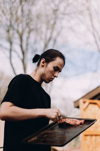 Young male adult placing steaks on barbecue.