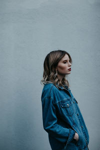 Side view of young woman standing against wall