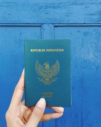 Cropped hand holding passport against blue wooden door