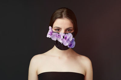 Portrait of woman wearing floral mask against black background