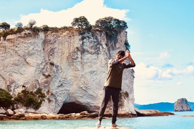 Man standing on rock formation by sea against sky