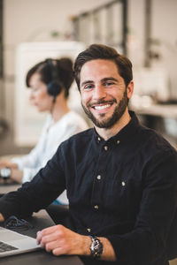 Portrait of smiling businessman sitting at desk in creative office