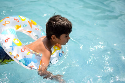 Happy indian boy swimming in a pool, kid wearing swimming costume along with air tube during day