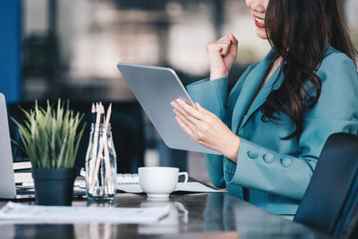 Midsection of woman using digital tablet while sitting on table