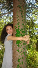 Portrait of smiling young woman standing against tree trunk in forest