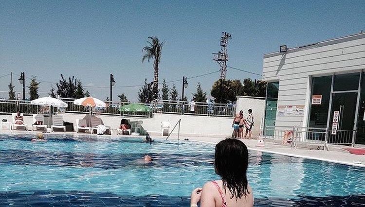 REAR VIEW OF PEOPLE IN SWIMMING POOL AGAINST BUILDINGS