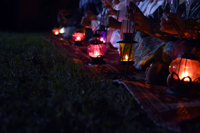 Low section of women holding lanterns while sitting outdoors at night