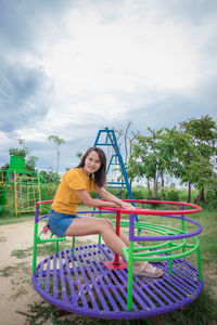 Portrait of smiling woman sitting colorful play equipment against sky