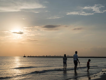 People standing on beach against sky during sunset