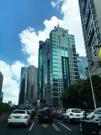 Cars on road by buildings in city against sky