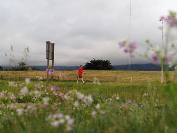 Woman walking on grassy field against cloudy sky