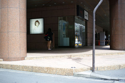 Woman walking on footpath by building in city