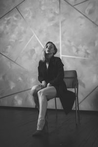 Portrait of young woman sitting on chair against wall