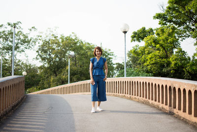 Young woman standing on bridge against sky in city