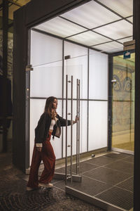Full length of woman entering through glass door