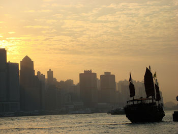 Sailboats in sea by buildings against sky during sunset