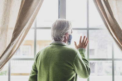 Rear view of man standing by window at home