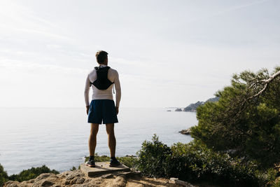 Rear view of man standing by sea against sky