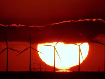 Silhouette of wind turbines against sunset sky