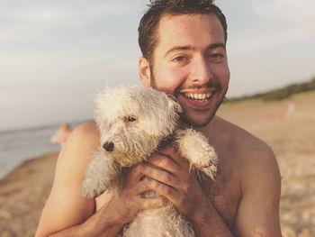 Portrait of happy young man holding cute puppy at beach