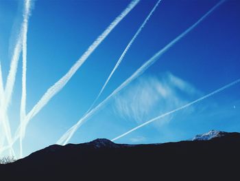 Low angle view of mountains against vapor trails in blue sky