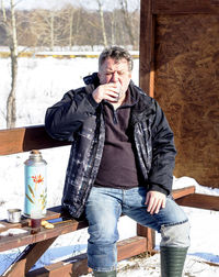 Man drinking drink while sitting on bench during winter