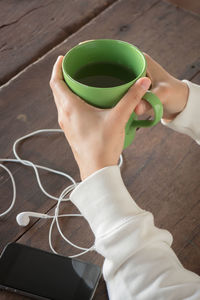Cropped hands of woman holding coffee cup with smart phone on table