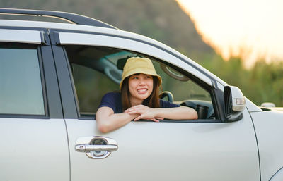 Portrait of a smiling young woman sitting on car