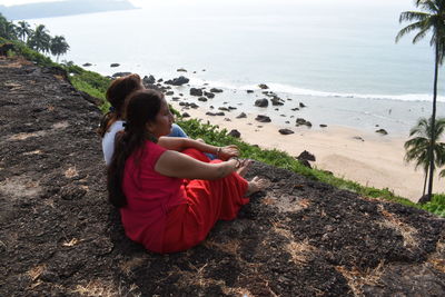 Rear view of woman sitting on rock at beach