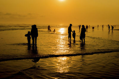 Silhouette people on beach against sky during sunset