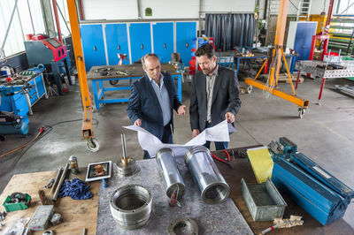 Two engineers with construction plan in front of hydraulic cylinder