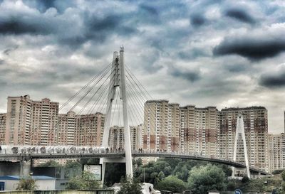 View of suspension bridge in city against cloudy sky