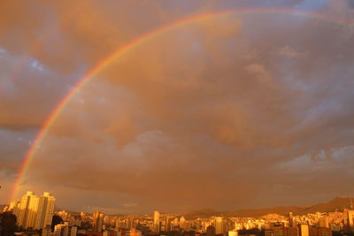 Rainbow over buildings in city against sky at sunset