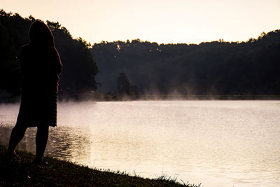 Silhouette woman standing by lake against sky during sunset